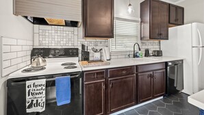 A modern kitchen with dark wooden cabinets, a white countertop, a built-in stove, and a dishwasher. - Clayton's 1910, Completely Restored Mill House, business-friendly weekday rates (Graham)