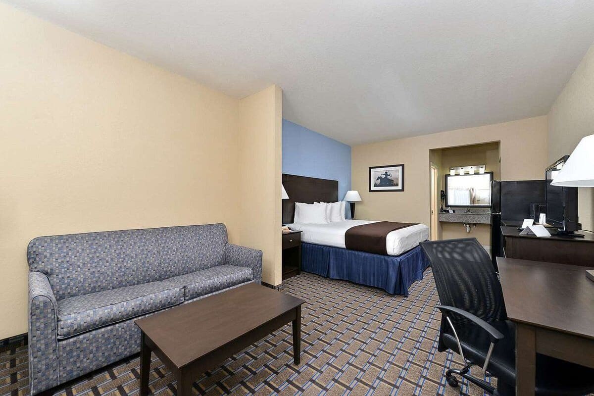 A hotel room with a sofa, a bed with a blue bedspread, a desk with a computer, and a television.