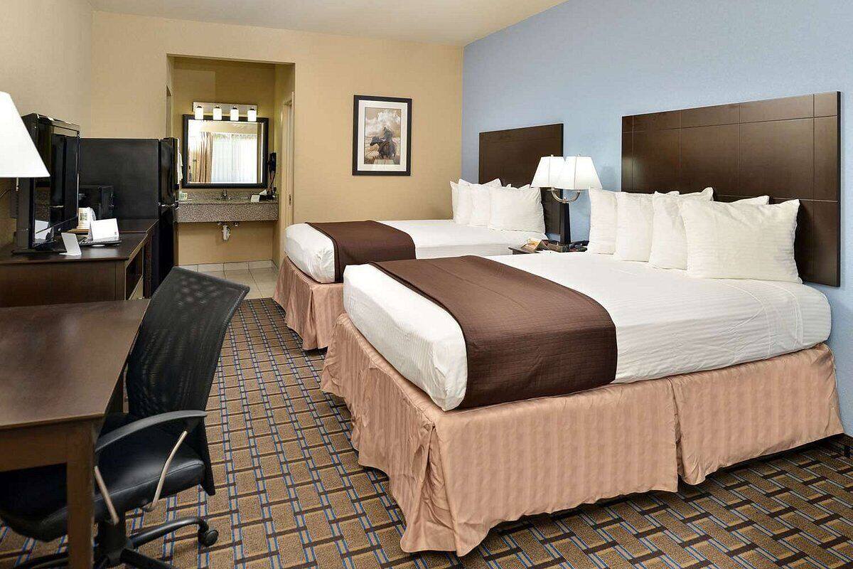 A hotel room with two beds, a desk, a chair, a mirror, and a framed picture on the wall.