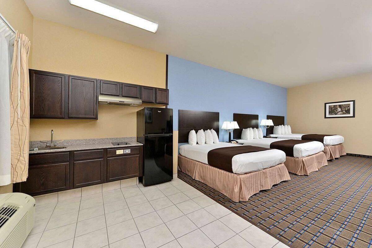A hotel room with a kitchenette, two beds, a large window, and a patterned floor.