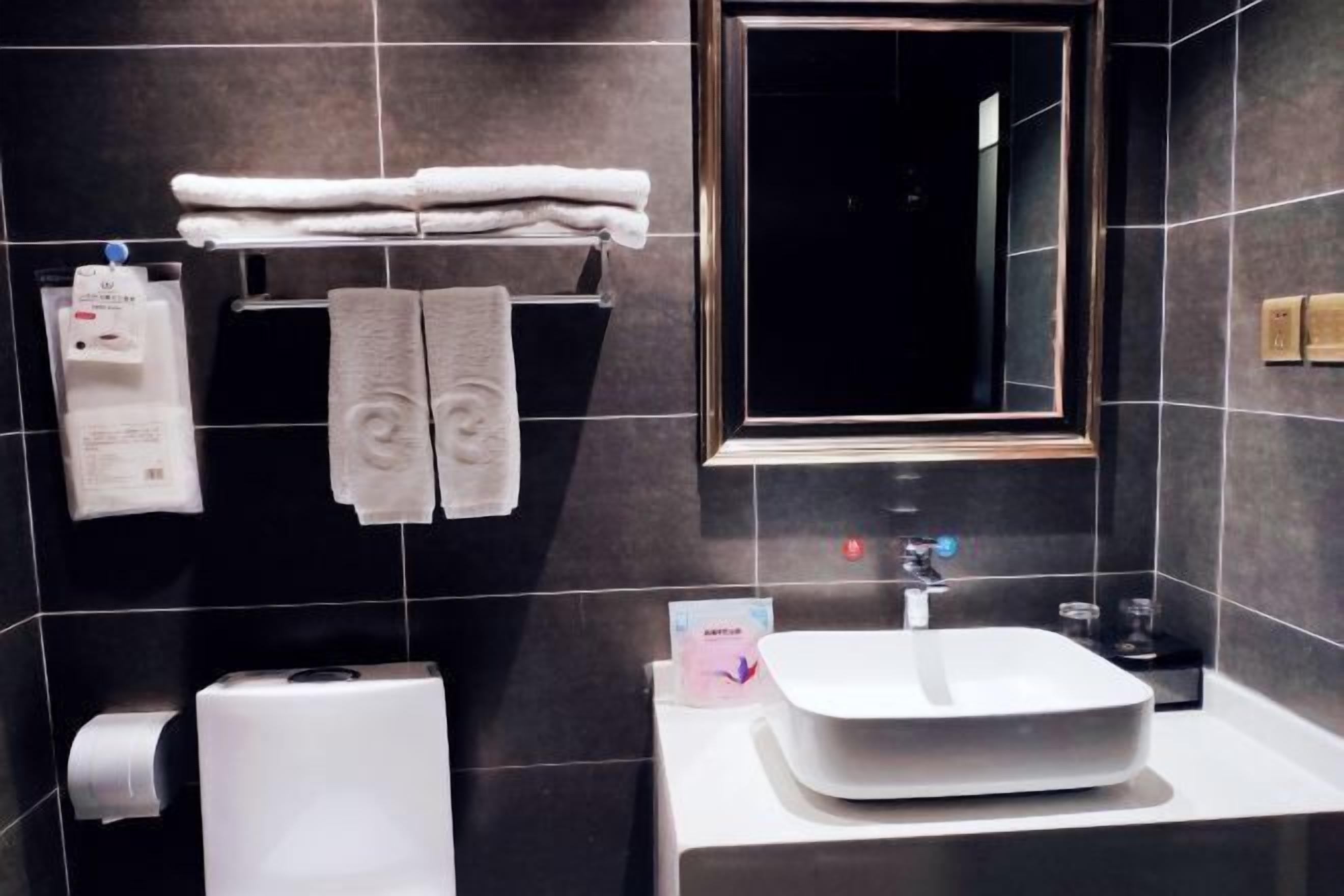 Un baño moderno con un espejo grande, un lavamanos blanco y dos toallas colgadas en un perchero.