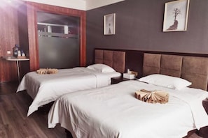 A hotel room with two beds, a wooden wardrobe, a bedside table, and a wall-mounted artwork.