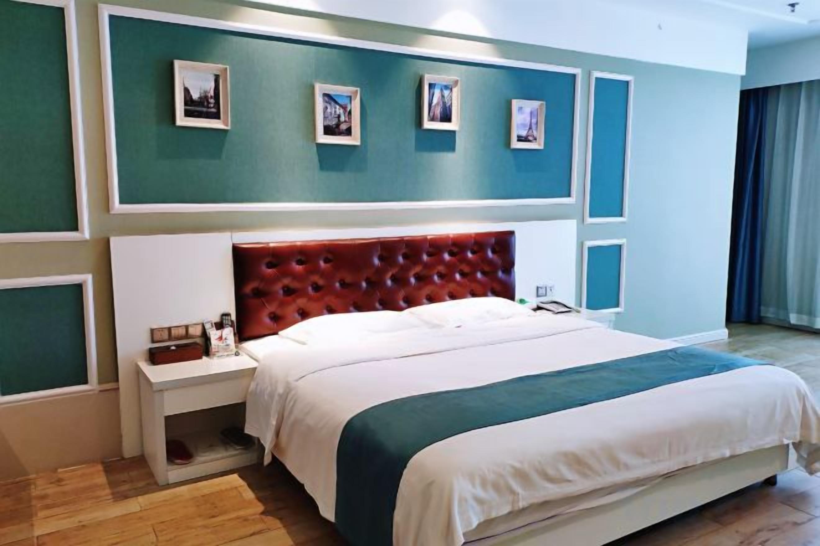 A hotel room with a large bed, a nightstand, a red upholstered headboard, and a wall with framed pictures.