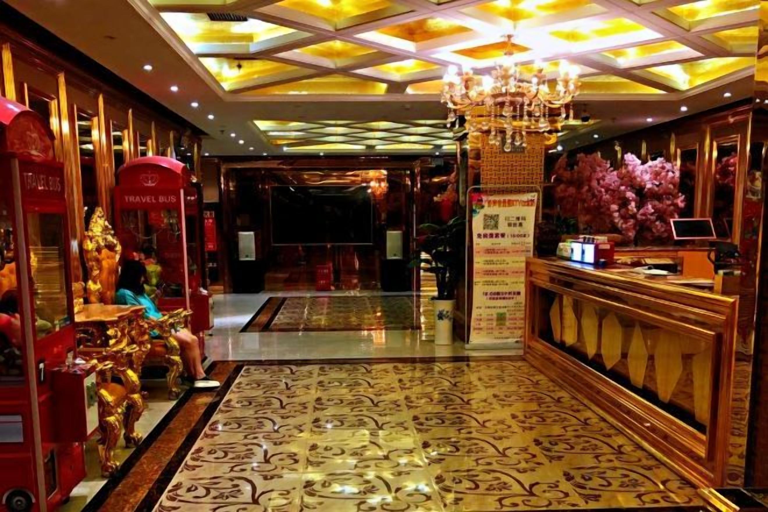 A hotel lobby with a reception desk, a chandelier, and a patterned carpet.