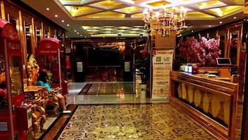 A hotel lobby with a reception desk, a chandelier, and a patterned carpet.