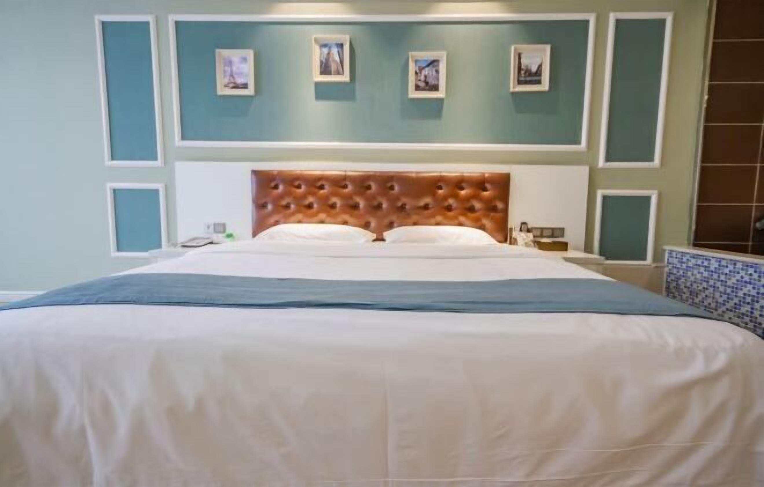 Une chambre d’hôtel avec un grand lit, une tête de lit en bois et un mur bleu orné de tableaux encadrés.
