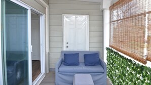 A balcony with a sliding glass door, a white door, and a blue sofa with cushions.