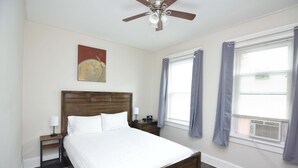 A neatly arranged bedroom with a wooden bed, a nightstand, a ceiling fan, and a window with curtains.