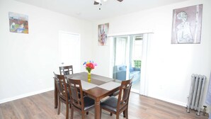 A dining room with a wooden table, four chairs, a vase with flowers, and artwork on the walls.