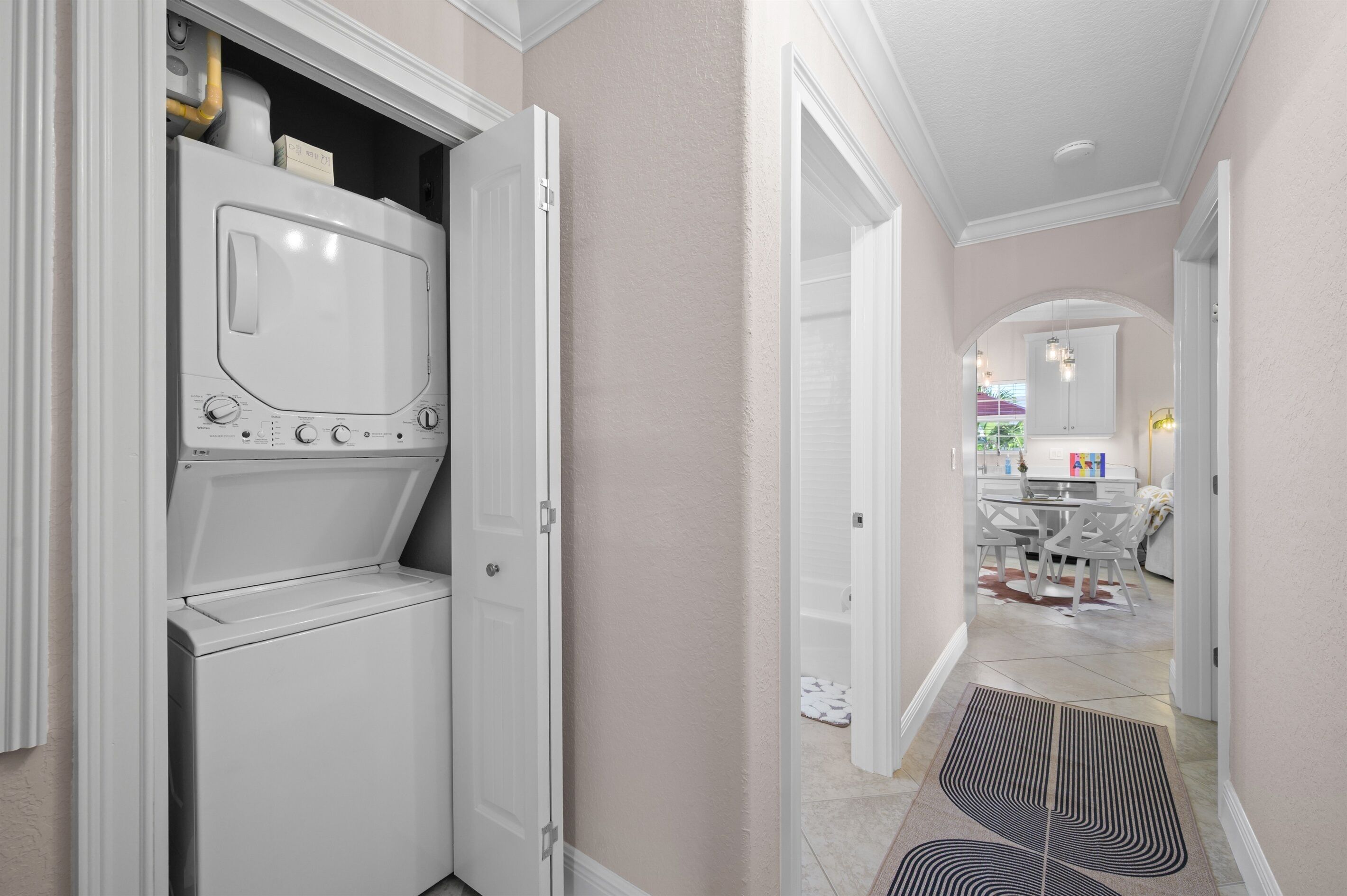 A laundry room with a washer and dryer, a hallway leading to a dining area with a table and chairs, and a door leading to another room.