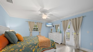 A bedroom with a bed, a ceiling fan, a television, a dresser, and a window with curtains.