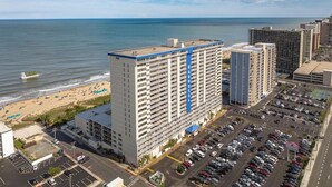 A high-rise hotel with a blue vertical stripe, a parking lot, and a beach in the background. - Oceanfront 2 Bed/2 Bath, Sleeps 6, Pools, Gym, Etc (Ocean City)