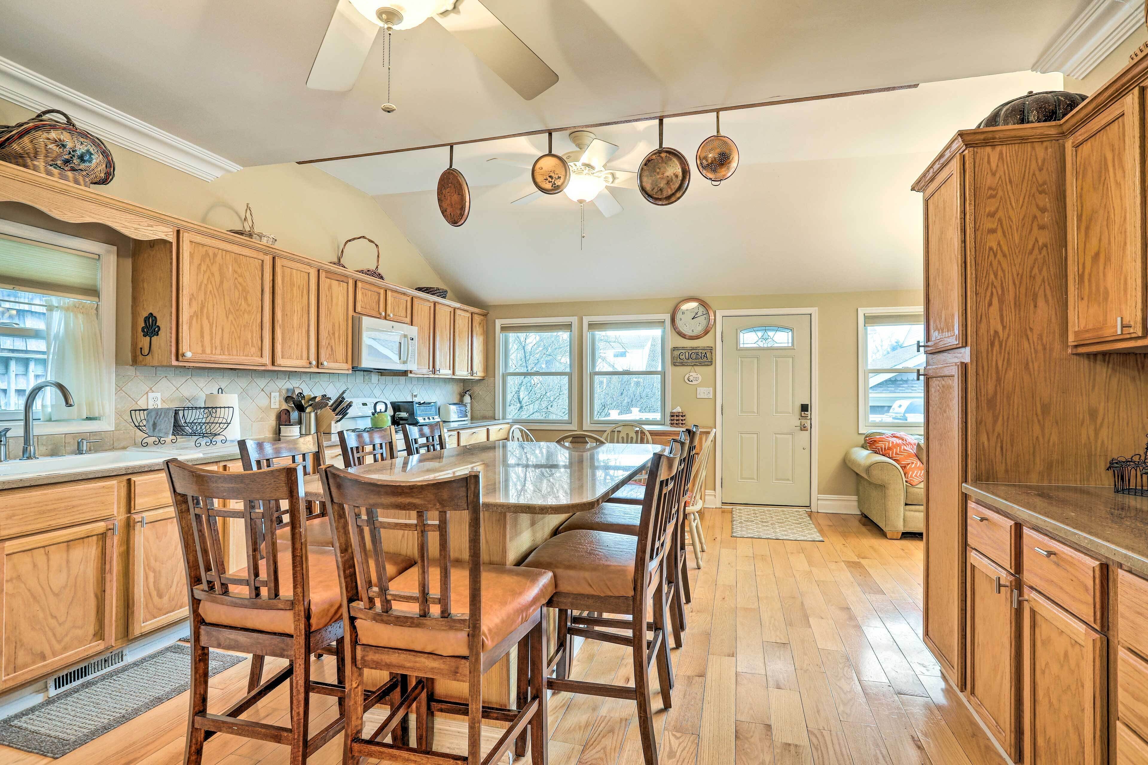 A spacious kitchen with wooden cabinets, a large island with chairs, and a ceiling fan.