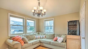 A corner living room with a sectional sofa, large windows, a chandelier, and a wooden cabinet. - Beautiful Spacious Beach Home, Private Deck & Grill, 5-min to Beach w/ Badges (Point Pleasant Beach)