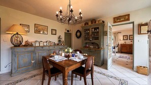 Een eetkamer met een houten tafel, stoelen, een kroonluchter en een kast met servies.