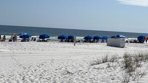 A beach with rows of blue umbrellas and beach chairs, a sandy shore, and the ocean in the background. - Newly Remodeled, Beachfront Condo, Sleeps Six, Resort Amenities! (Orange Beach)