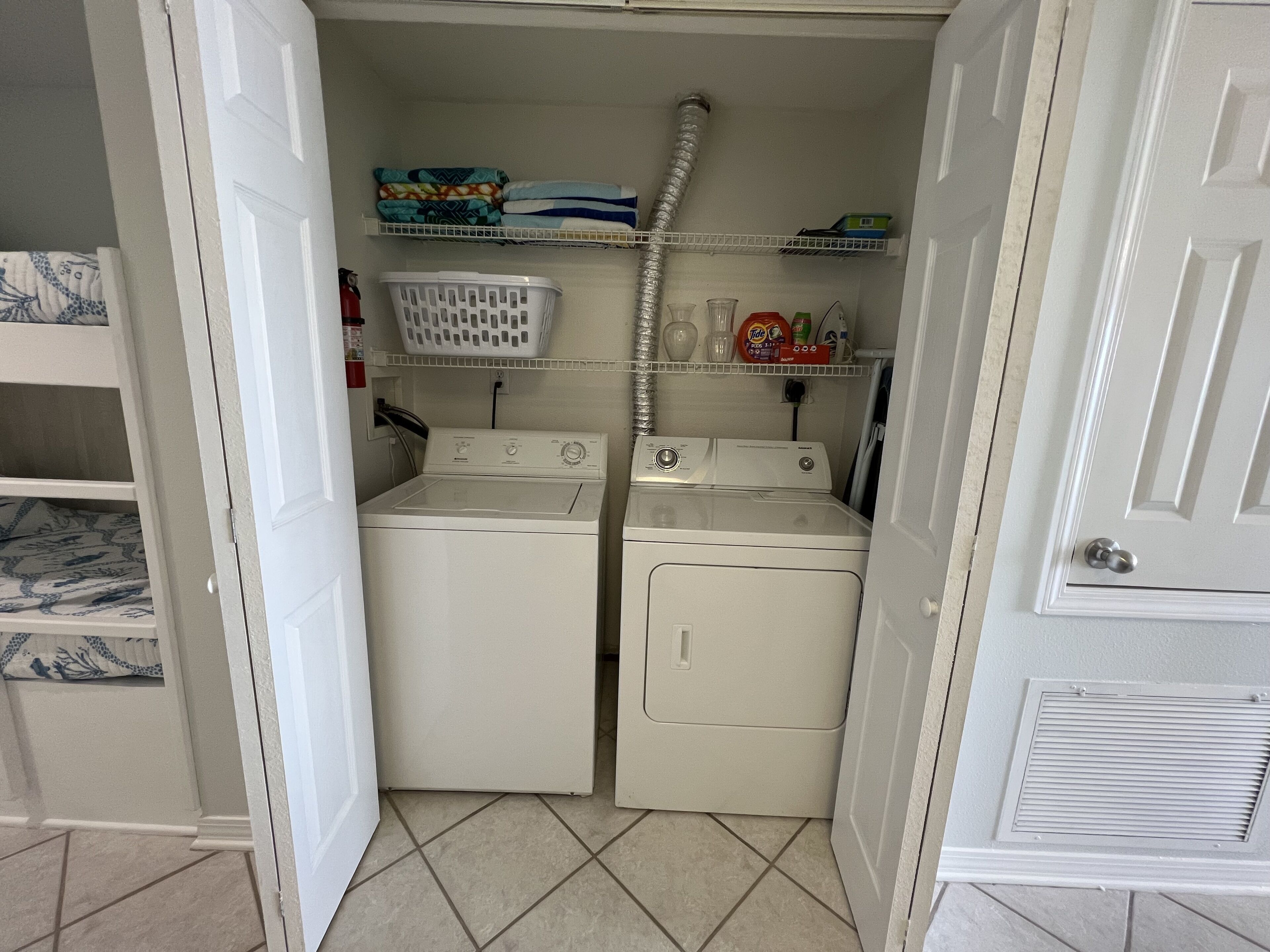 A laundry room with two stacked washers and dryers, a shelf with laundry detergent, and a basket.