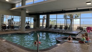 An indoor swimming pool with clear views of the outdoors, including a palm tree and a fenced area. - Newly Remodeled, Beachfront Condo, Sleeps Six, Resort Amenities! (Orange Beach)