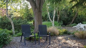Two black metal chairs placed on a gravel path in a garden setting with trees and greenery. - Countryside  caravan accomodation (Cutnall Green)