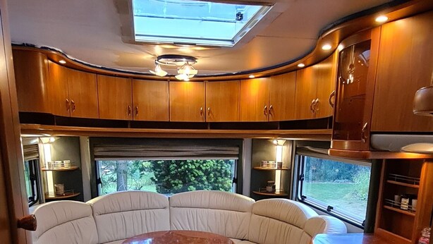 A cozy RV interior with a curved seating area, wooden flooring, and built-in cabinets. - Countryside  caravan accomodation (Cutnall Green)