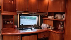 A compact kitchen with wooden cabinets, a built-in stove, and a window with a view of greenery. - Countryside  caravan accomodation (Cutnall Green)