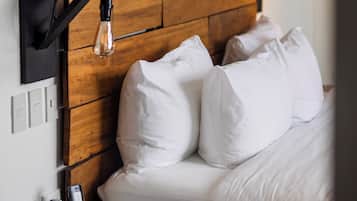 A neatly made bed with white linens, a wooden headboard, a bedside table with a phone and papers, and a wall-mounted light fixture.