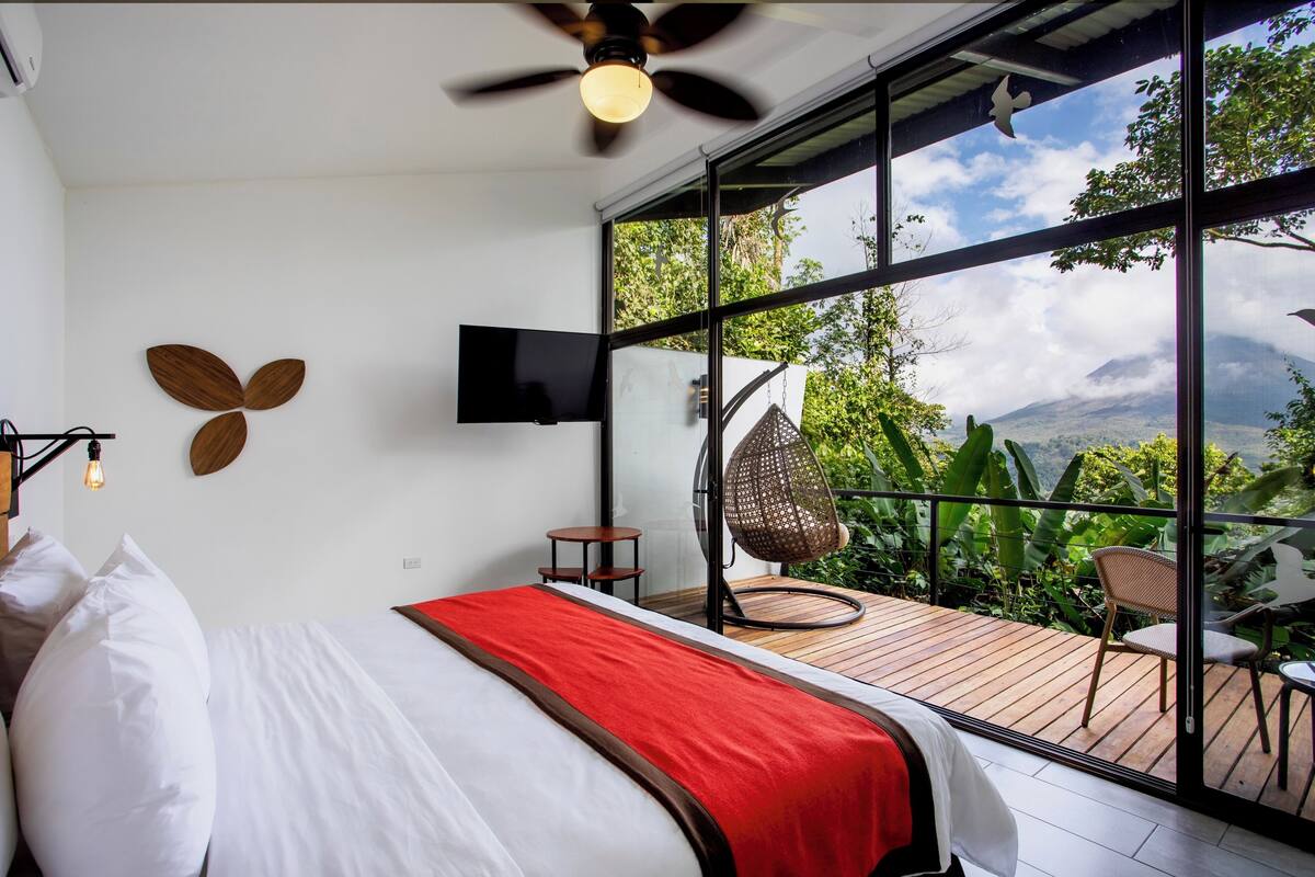 Ein Schlafzimmer mit großem Fenster, einem Bett, einem Deckenventilator und einem Fernseher.