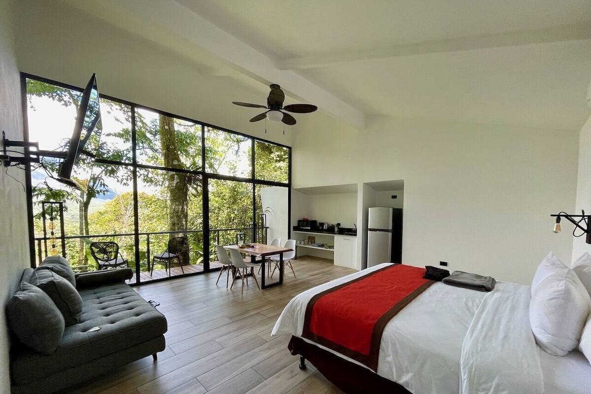 Ein modernes Schlafzimmer mit einem großen Bett, einer Couch, einem Esstisch und einer Küchenzeile.
