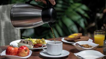 A breakfast setting with a coffee pot pouring into a cup, surrounded by plates of food and a glass of orange juice.