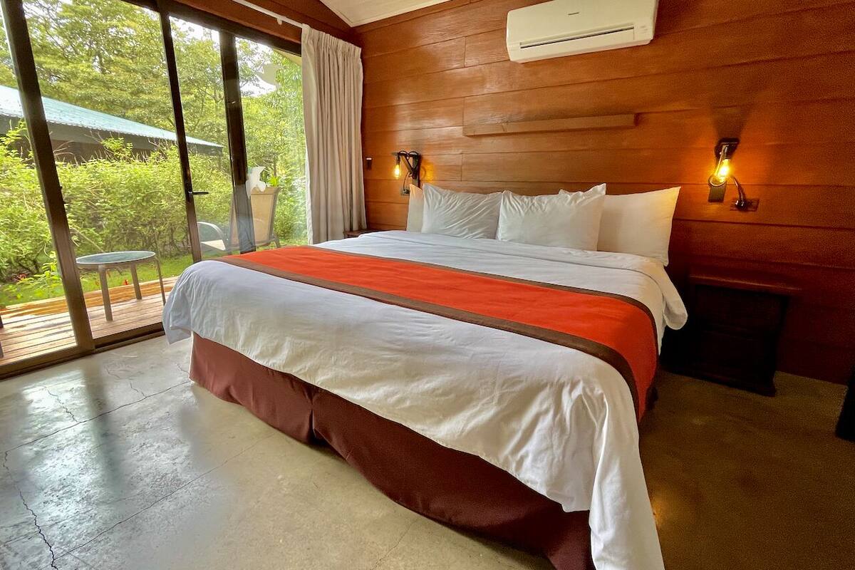Ein Schlafzimmer mit einem großen Bett, Holzwänden, einer Klimaanlage und Blick durch eine Glastür.