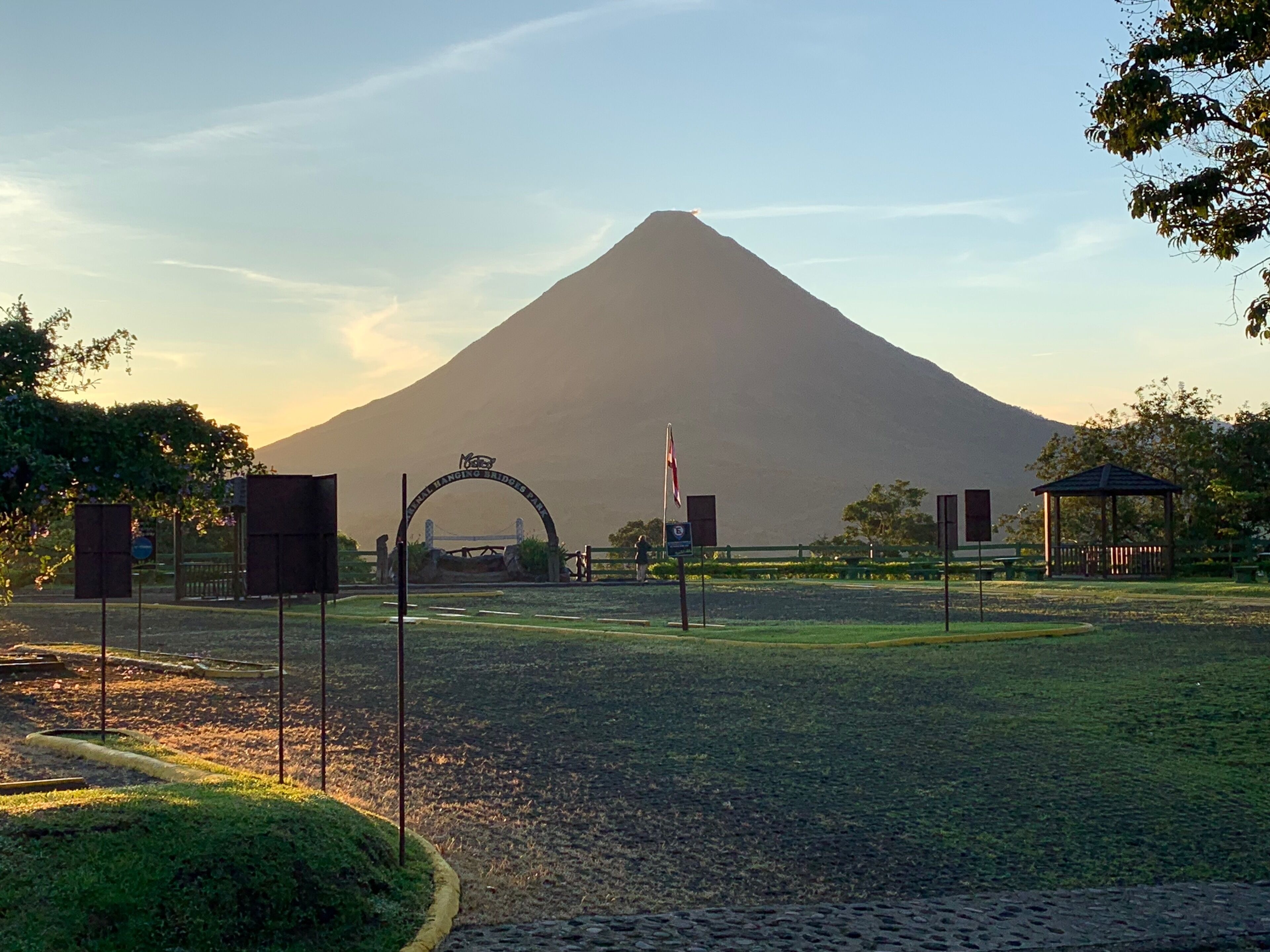 A paved area with a large archway, a flagpole, and a gazebo.