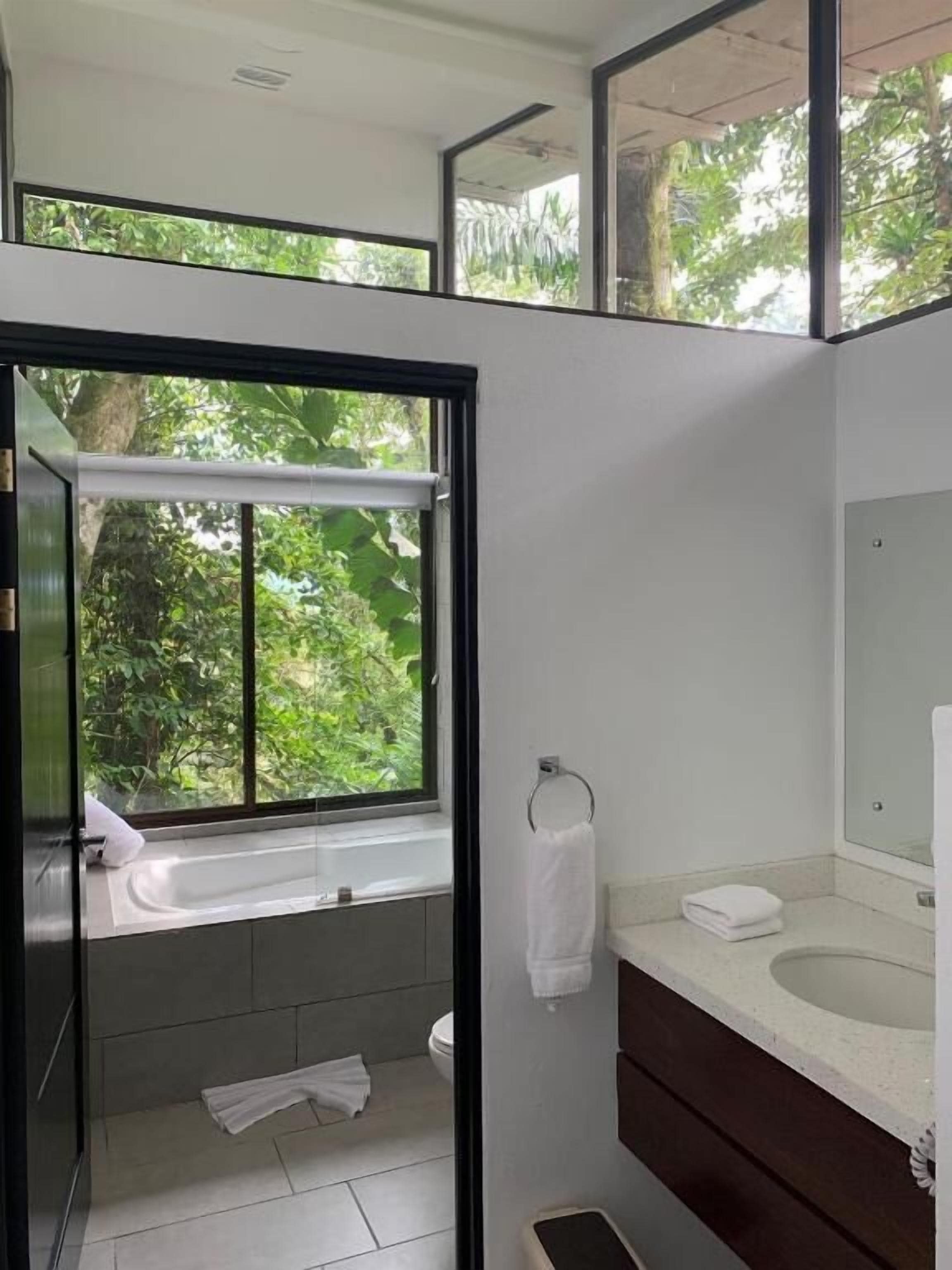 Une salle de bain moderne dotée d’une grande fenêtre, d’une baignoire, d’un lavabo et de toilettes.