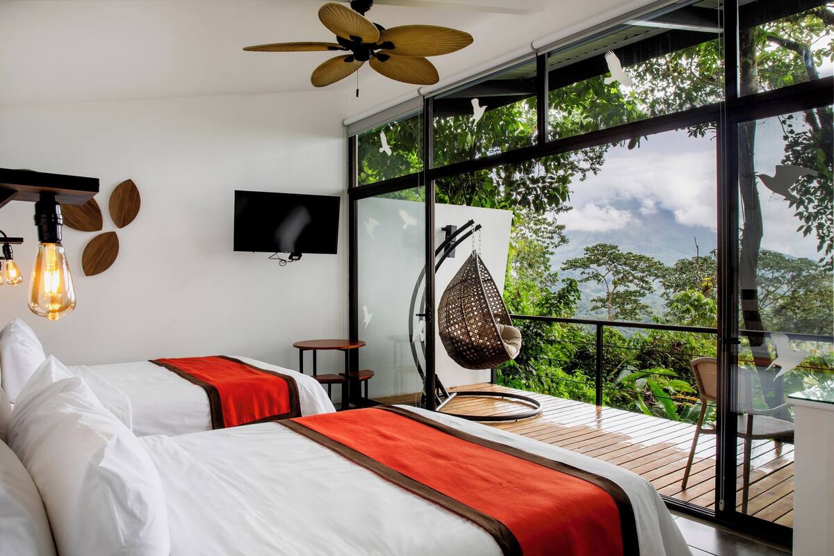 Ein modernes Schlafzimmer mit zwei Betten, einem Fernseher und einem Balkon mit Blick auf Grünflächen.