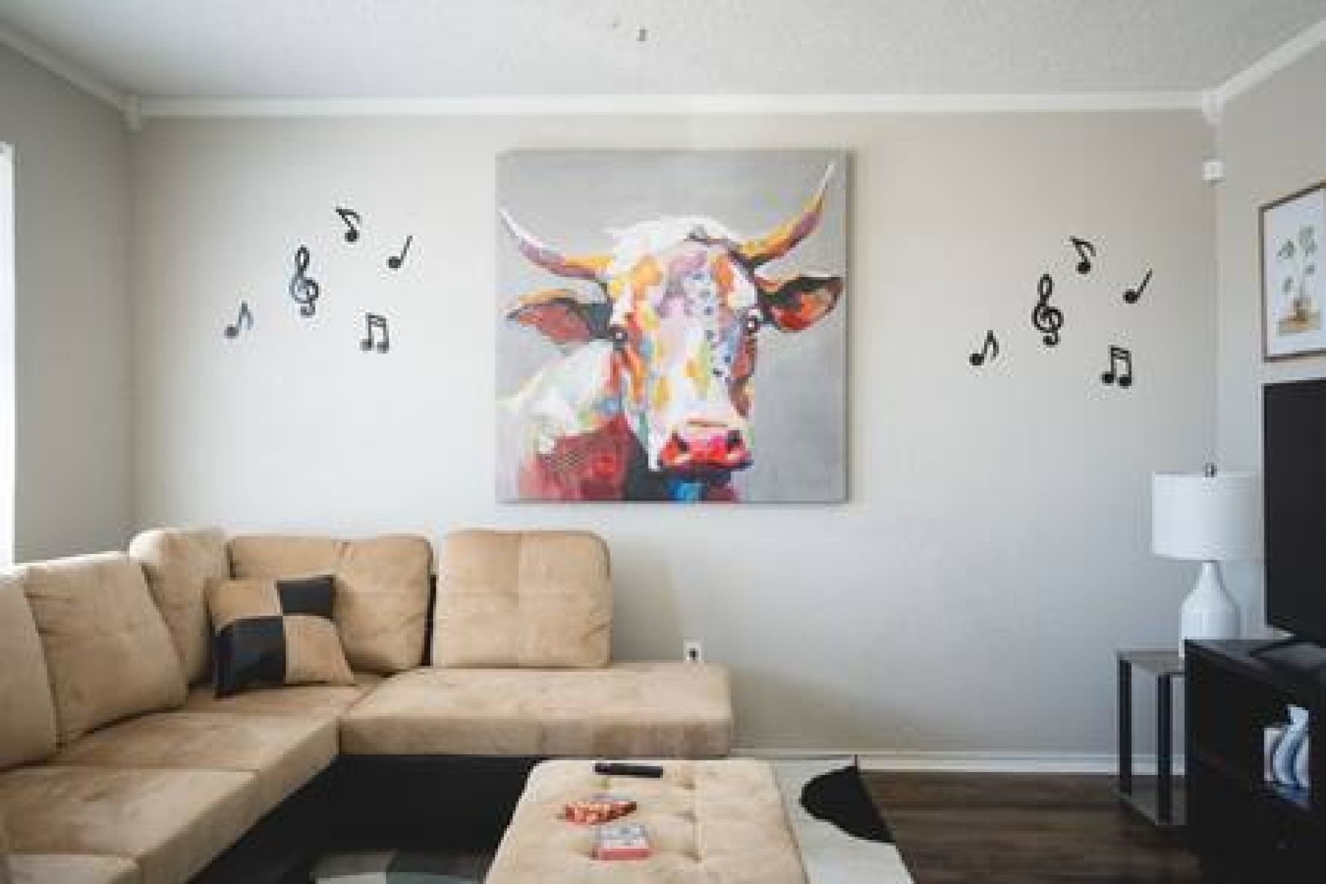 A living room with a beige sofa, a coffee table, and a colorful cow painting on the wall.