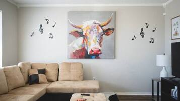 A living room with a beige sofa, a coffee table, and a colorful cow painting on the wall.