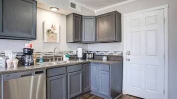 A kitchen with grey cabinets, a dishwasher, a coffee maker, and a white door.