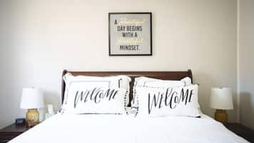 A neatly made bed with two pillows, each with the word 'WELCOME' on them, and a framed inspirational quote on the wall above.