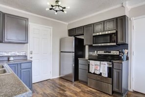 A kitchen with grey cabinets, a stainless steel refrigerator, a microwave, and a stove.