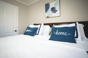 Une chambre d’hôtel avec un lit, des oreillers ornés du mot « chez soi », une porte et un tableau mural.