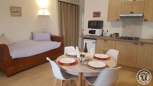 A compact living space with a bed, a dining table set for four, a microwave, a small refrigerator, and a gas stove. - Gîte St Michel - SAINT-CLEMENT-LES-PLACES (SAINT-CLEMENT-LES-PLACES)