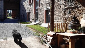 A stone building with a paved courtyard and a dog walking on a leash. - Gîte St Michel - SAINT-CLEMENT-LES-PLACES (SAINT-CLEMENT-LES-PLACES)