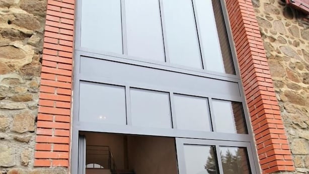 A modern building with a stone facade, a large glass entrance, and a visible staircase leading to an upper level. - Gîte St Michel - SAINT-CLEMENT-LES-PLACES (SAINT-CLEMENT-LES-PLACES)
