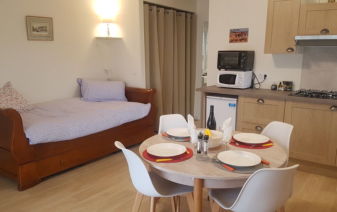 Un espace de vie compact comprenant un lit, une table à manger pour quatre personnes, un four à micro-ondes, un petit réfrigérateur et une cuisinière à gaz.