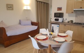 Een compact woongedeelte met een bed, een eettafel voor vier personen, een magnetron, een kleine koelkast en een gasfornuis.