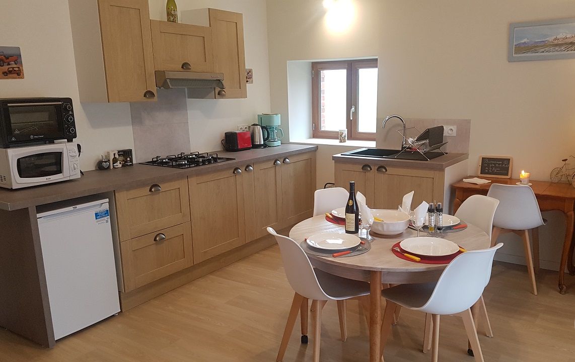 A compact kitchen with wooden cabinets, a microwave, a gas stove, and a sink. There is a dining table with chairs and a small refrigerator.
