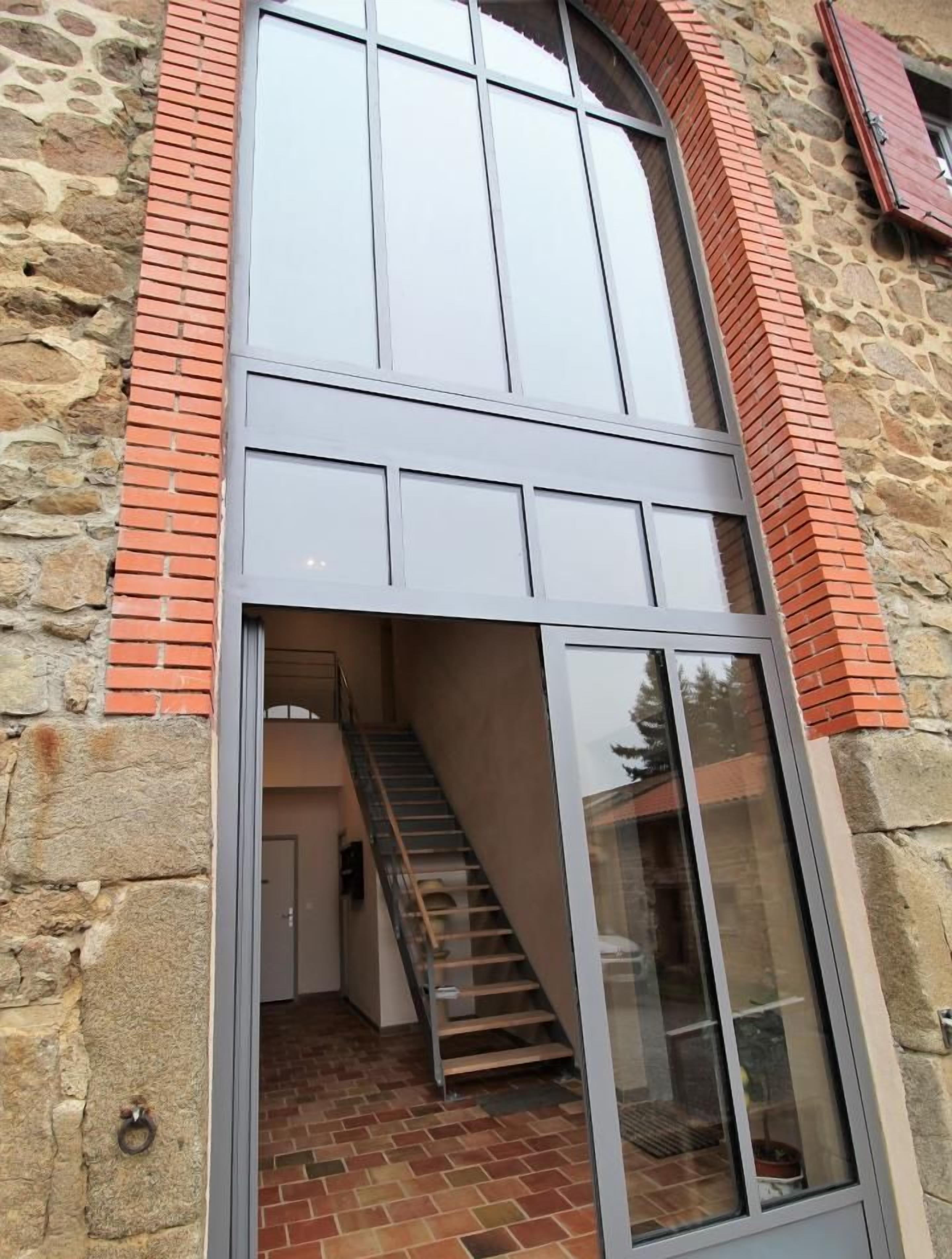 Een modern gebouw met een stenen gevel, een ruime glazen ingang en een open trap die naar een hoger gelegen verdieping leidt.