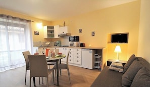 Un espace de vie compact comprenant un coin cuisine, un coin repas et un téléviseur fixé au mur.