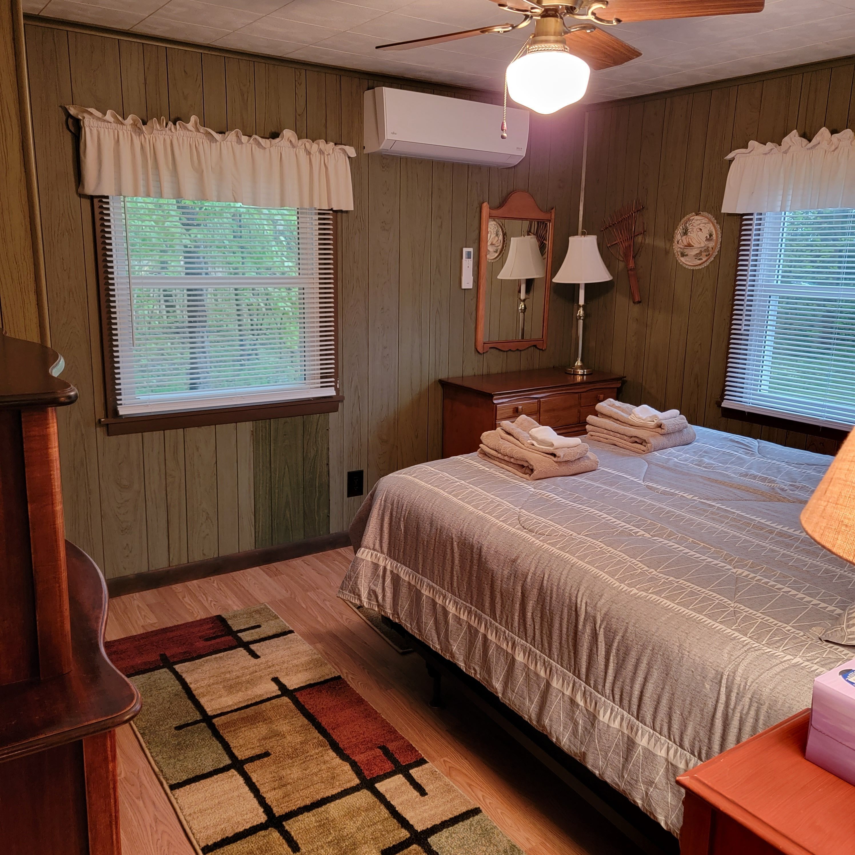 A bedroom with a bed, a nightstand, a dresser, a mirror, a lamp, and a ceiling fan.