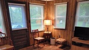 A cozy cabin interior with wooden walls, a wooden floor, a sofa, a small table with a lamp, a television, and a window with blinds. - In the narrows on Lake Leelanau, pet friendly, sleeps 8, and a dock! (Lake Leelanau)