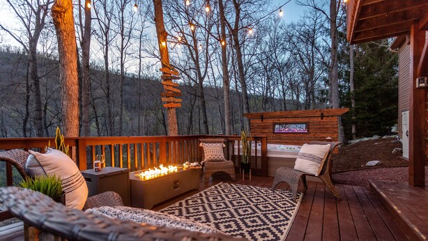 A wooden deck with outdoor seating, a fire pit, and a wooden cabin structure.